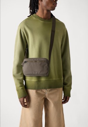 Olive green sweatshirt with a crew neckline, paired with oversized beige pants. A small brown crossbody bag with zipper details is worn.