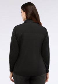 Camicia nera a maniche lunghe con colletto, dalla texture liscia e con polsini a bottoni. Presenta un design con spalle a yoke e arriva sotto la vita.