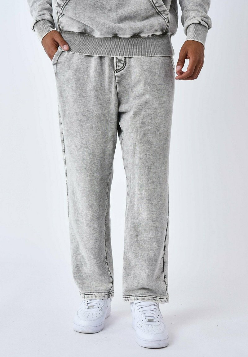 Pantalones de chándal de algodón gris con una textura desgastada, cintura elástica, bolsillos laterales y corte recto, combinados con zapatillas blancas.