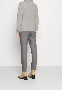 Pull gris en maille à col montant, associé à un pantalon noir et blanc à motif pied-de-poule et des bottines beiges à talons carrés.