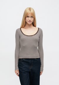 Hosszú ujjú felső, amelyen vízszintes barna és fehér csíkok találhatók, kerek nyakkivágással és bordázott textúrával. Magas derekú sötét farmerrel párosítva.