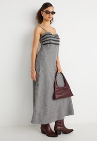 Γυναίκα που φοράει ασπρόμαυρο καρό φόρεμα χωρίς μανίκια, μαύρα γυαλιά ηλίου, κρατάει σκοτεινό μωβ τσάντα και φοράει μπότες που ταιριάζουν.