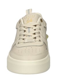Beige sneaker met een bovenwerk van textuurleer, vetersluiting, geperforeerde neus en een crèmekleurige rubberen zool. Is voorzien van een gouden accentlogo.