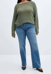 Olijfgroene gebreide trui met een losse pasvorm en wijde halslijn, gecombineerd met lichtblauwe flare jeans en zwarte puntige ballerina's.