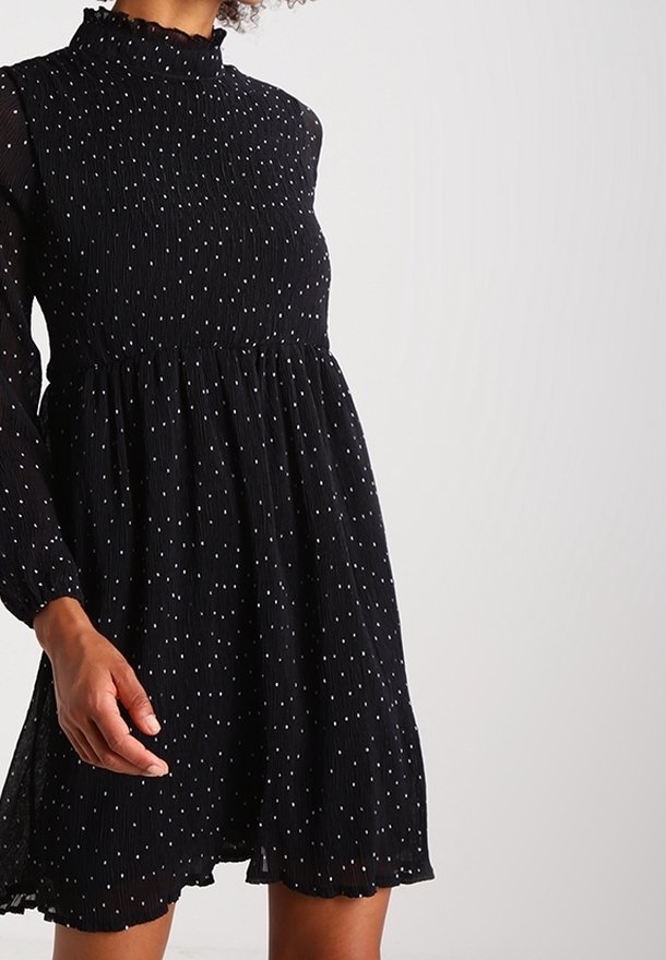 Black dress with a high ruffled neck, long sheer sleeves, and a flowing skirt, featuring white polka dots throughout.