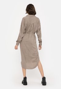 Brown checkered shirt dress with long sleeves, a belted waist, and high slit detail. Paired with black ankle boots. Soft fabric texture.