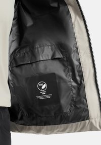 Fodera interna nera di una giacca con una tasca visibile. La tasca contiene un'etichetta che riporta la dicitura "700 Piuma Naturale" con un'icona di una piuma.