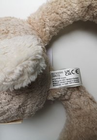 Tan plush toy featuring soft fur texture, embroidered detailing, and a label indicating eco-friendly production.