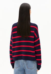 Marineblauwe trui met rode horizontale strepen, voorzien van een losse fit en geribbelde textuur, gecombineerd met lichtblauwe hooggetailleerde jeans.