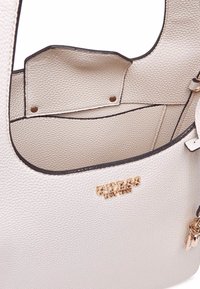 Borsa a tracolla in pelle bianca con texture, dalla forma flessibile, con tasca interna e decorazione in metallo dorato. Bordo liscio e cuciture a contrasto.
