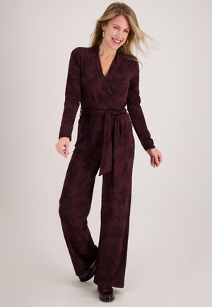 Bruine wikkeljumpsuit met lange mouwen, ceintuur in de taille en bloemmotief. Gemaakt van zachte stof, met een broekspijp met wijde pijpen en een gladde textuur.