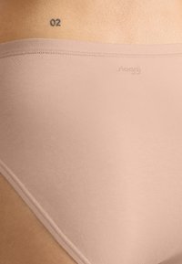 Intimo Sloggi beige con una texture liscia e design senza cuciture, caratterizzato da un branding minimale e un taglio a vita bassa.