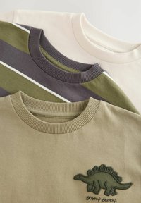 Drei kurzärmelige Hemden: beige mit geripptem Kragen, olivgrün mit Streifen und ein grünes Hemd mit Dinosaurier-Stickerei. Aus weichem Baumwollmaterial.
