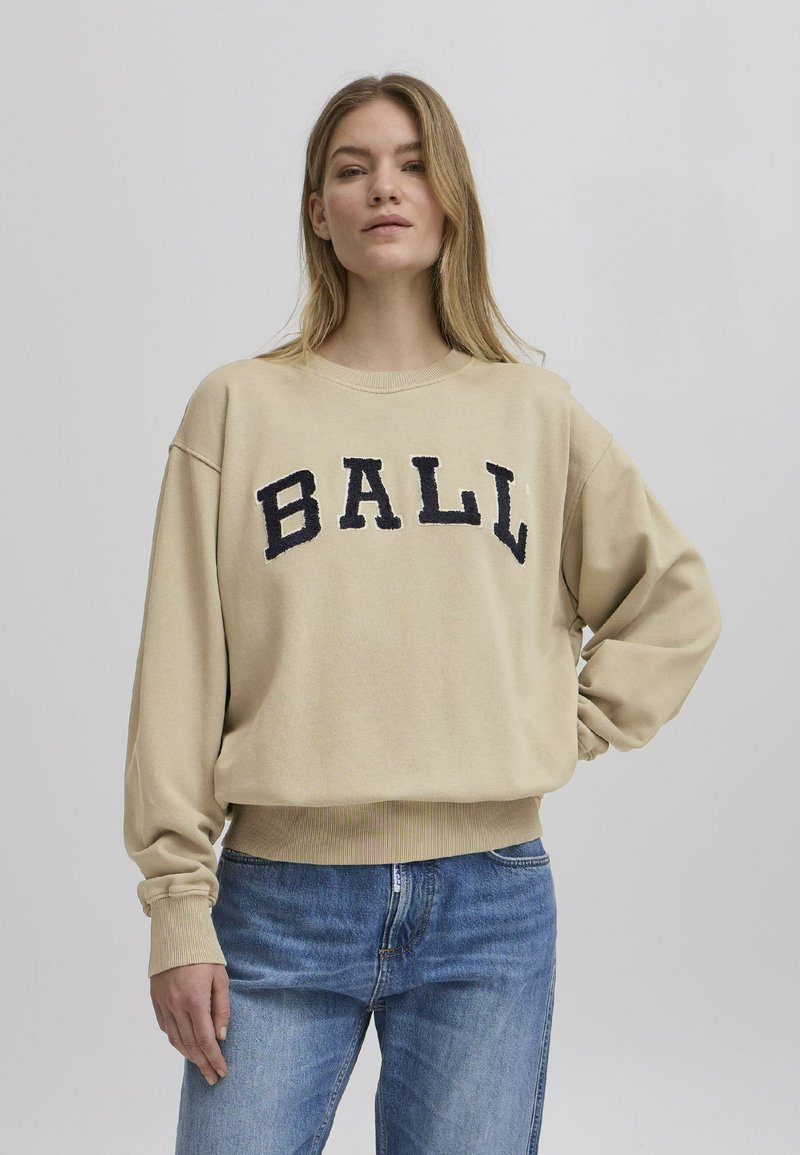 Beige avkortet genser med oversized passform, med "BALL" i marineblå broderte bokstaver på forsiden. Ribbestrikkede mansjetter og kant.