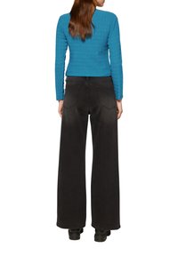 Haut à manches longues texturé bleu avec un col rond associé à un pantalon large à taille haute noir, doté de deux poches arrière.