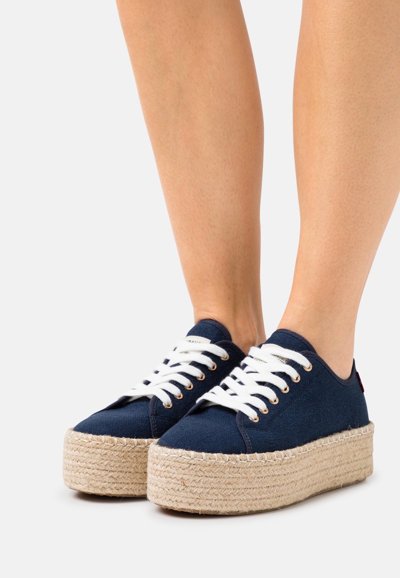 Navy canvas sneakers with white laces, featuring a jute rope platform sole. Rounded toe and simple design with no additional embellishments.