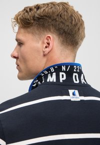 Navy blue polo shirt with white stripes, featuring a patterned collar in blue and white, and a brand tag at the back neck.