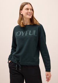 Mörkgrön sweatshirt med rundad halsringning och sänkt axelsöm. Har stor texten "JOYFUL" över framsidan och en dragsko i fållen.