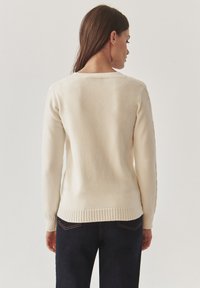 Crème-kleurige trui met lange mouwen, geribde onderrand en ronde halslijn. Zachte textuur, eenvoudig ontwerp en eenvoudige achterkant.