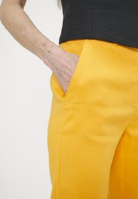 Pantalon en lin jaune avec une texture lisse, poches latérales et coutures soigneusement cousues, associé à un haut noir ajusté.