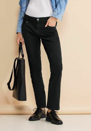 Pantalons noirs avec une coupe droite, fermeture à bouton et poches avant. Associés à des chaussures noires et un sac fourre-tout noir.