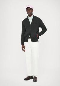 Tmavě šedý žebrovaný kardigan se zipem, spojený s modrobílým pruhovaným tričkem, bílými kalhotami a růžovou čepicí. Hnědé obutí.