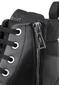 Baskets montantes en cuir noir avec fermeture éclair argentée, lacets tressés, étiquette de marque sur la cheville, et un panneau en tissu texturé.