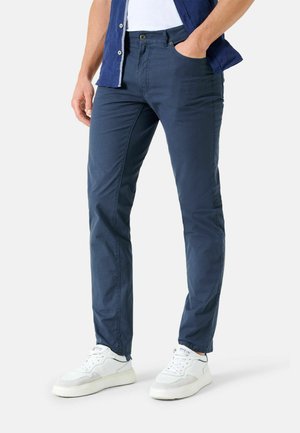 Navy blue pants made of lightweight fabric, feature front pockets, slim fit design, and are styled with white sneakers.