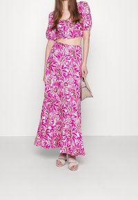 Top court floral rose assorti à une jupe longue. Présente des manches bouffantes, une taille cintrée et une silhouette fluide. Design épuré.