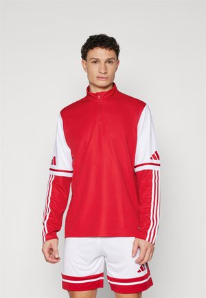 Rød atletisk pullover med halvvending, hvide accenter på ærmerne og Adidas-striber. Sammen med hvide shorts med røde striber.