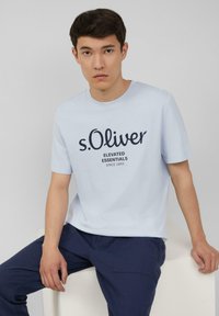 Lichtblauw katoenen T-shirt met een marineblauw logo en de tekst "s.Oliver Elevated Essentials sinds 1969," ronde halslijn en korte mouwen.