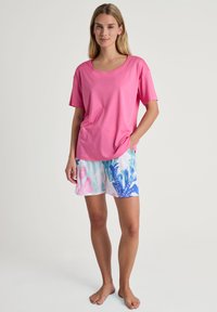 Roze T-shirt met korte mouwen van een zachte stof, gecombineerd met gecamoufleerde shorts met blauwe en roze bloemmotieven tegen een witte achtergrond.
