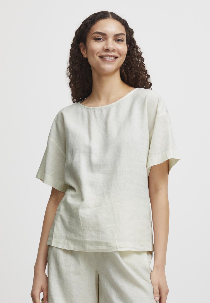 Haut en lin vert clair avec un col rond et des manches courtes, présentant une coupe décontractée et une texture subtile. Pas de motifs ou d'accents marquants.