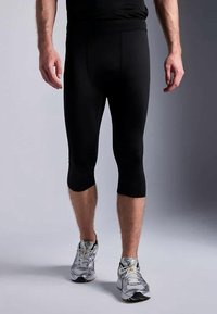 Svarte atletiske capri leggings med en tettsittende design, midt på leggen lengde, laget av elastisk materiale, kombinert med grå løpesko.