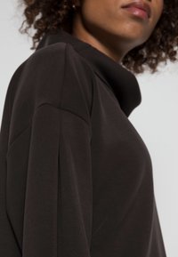 Černý dlouhý rukáv s vysokým límcem, s hladkým povrchem a uvolněným střihem. Jemné šití na rukávech.