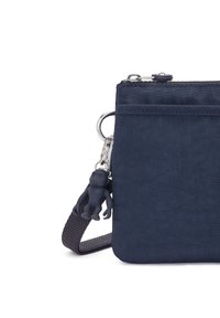 Marinblått tyg crossbody-väska med en strukturerad yta, silverfärgad hårdvara och en gummimonkey-charms fäst vid dragkedjan.