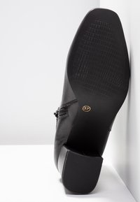 Schwarzer Absatzschuh mit glattem Lederoberteil und strukturiertem Gummisohle. Größe 37 ist auf der Sohle angegeben. Quadratisches Design des Absatzes.