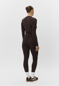 Hnedá súprava s dlhým rukávom a legínami, vyrobená z elastického materiálu. Oblečenie má priliehavý strih s minimálnymi viditeľnými švami.