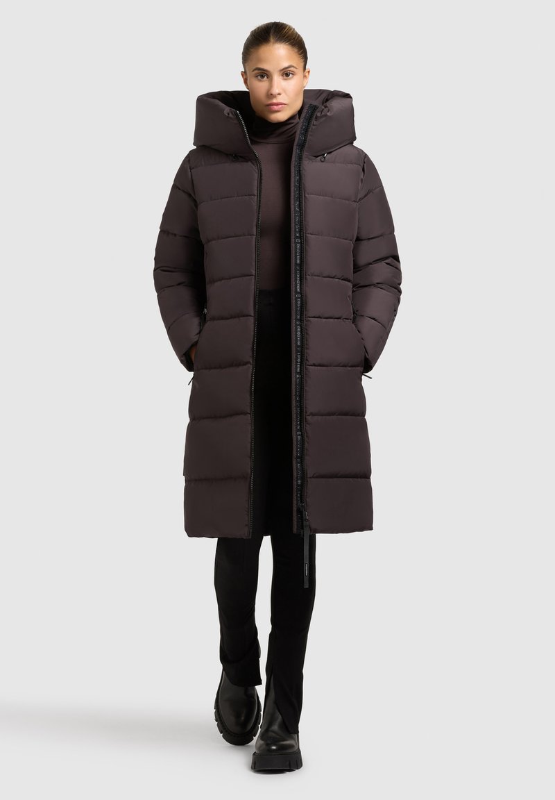 Donker pufferjack met een capuchon, voorzien van een ritssluiting, gestikt ontwerp en zijzakken. Draag het over een strakke top en smalle broek.