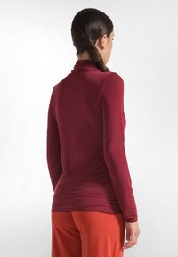 Bordeaux langmouwen turtleneck top met een gladde textuur, aansluitend ontwerp en gedrapeerd detail bij de taille, gecombineerd met oranje broek.