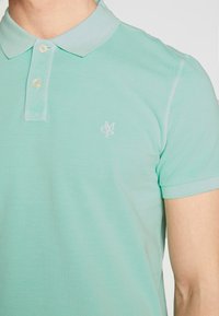 Jasnozielona koszulka polo z teksturowanego materiału, z klasycznym kołnierzem, plisą z dwoma guzikami i subtelnym haftowanym logo na piersi.
