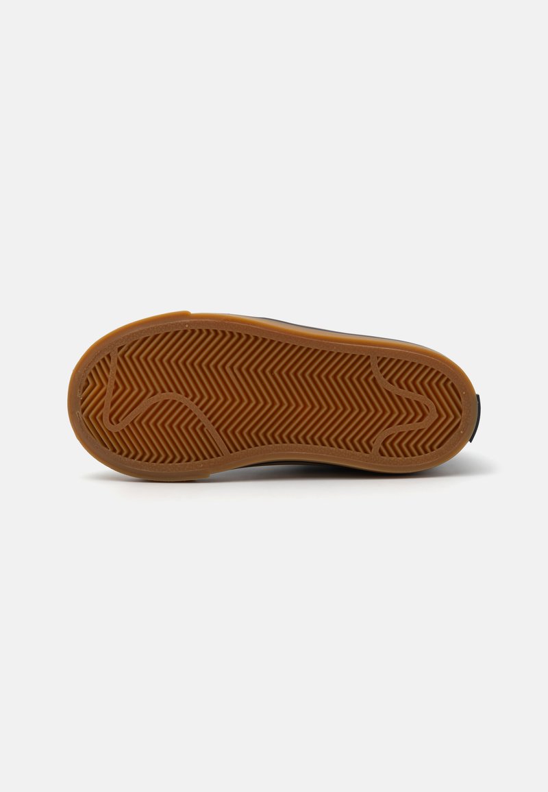 Semelle en caoutchouc marron avec un motif en chevrons, bords arrondis et une zone noire lisse au niveau du talon. Design épuré et minimal.