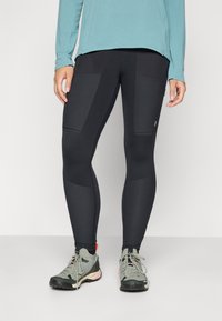 Zwarte sportlegging met een gladde textuur, voorzien van zijzakken en contrasterende panelen. Gecombineerd met grijze wandelschoenen.