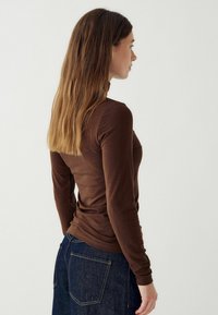 Barna, hosszú ujjú, testhez simuló felső, sima textúrával, rugalmas anyagból készült, kék farmernadrággal párosítva, amely hátul zsebekkel rendelkezik.