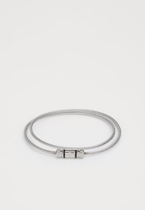 Bracelet en câble argenté avec un design à double boucle, accent central noir et extrémités en métal texturé pour un maintien sécurisé.