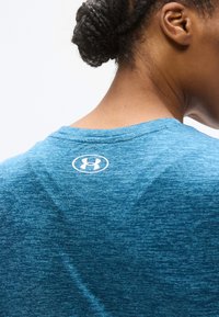 Μπλε αθλητική μπλούζα με υφασμάτινο, μαρκαρισμένο σχέδιο, στρογγυλή λαιμόκοψη και λευκό λογότυπο στην πλάτη κοντά στον λαιμό.