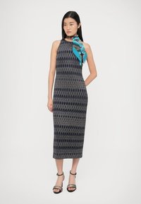 Tamsiai mėlyna ir smėlio spalvos be rankovių suknelė su tiesiu kirpimu, papuošta žalsvu šaliku ir juodais bateliais su dirželiais.