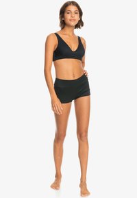 Svart trenings-BH med brede stropper og dyp V-hals, kombinert med matchende høyt midjerte shorts. Glatt stoff med en tettsittende silhuett.