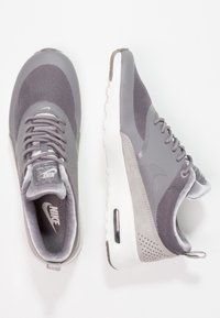 Nike Air Max sneakers med en grå mesh-övre, mockadetaljer, snören och en vit mellansula med synlig luftkuddar.