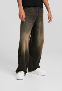 Mörka denimbyxor med vida ben som har en gradvis blekning från mörk till ljus, med synlig sömnad och sliten textur. Också i kombination med vita sneakers.